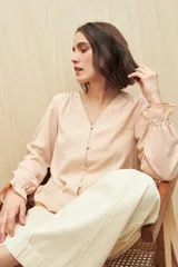 Camisa marrón de manga larga con escote en V y botones forrados al tono en el frente. Destaca por su textura sutil y por el detalle de frunces con volados en la parte inferior.