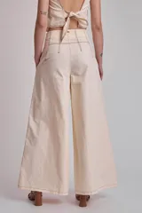 Pantalón negro de tiro alto, corte ancho y largo, con pliegues frontales y pespuntes contrastantes en blanco en la cintura y bolsillos.