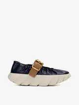 Zapato de cuero azul marino con correa marrón con hebilla dorada y suela de goma blanca con diseño ondulado.