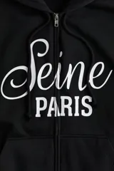 Campera negra con capucha y cierre frontal, con bolsillo tipo canguro y estampado blanco con la inscripción 'Seine Paris'.