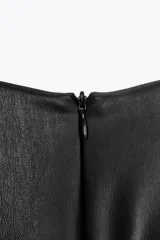 Vestido midi negro de efecto piel, con cuello redondo y sisa. Tiene abertura en la espalda y cierre trasero con cremallera oculta.