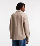 Camisa beige de tricolina texturizada, corte amplio, manga larga y abotonada al frente.