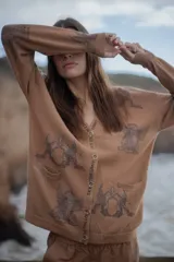 Cárdigan color marrón claro con estampado de aves, lunas y estrellas. Tiene escote en V, cierre con botones y bolsillos delanteros.
