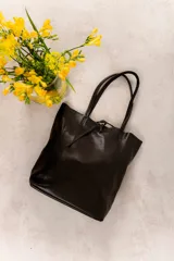 Bolso tote grande de cuero negro con doble asa larga y cierre superior con tira de cuero. Diseño minimalista y atemporal.
