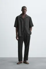 Pantalón negro de corte amplio, con textura acanalada, cintura elástica ajustable con cordón, bolsillos laterales y traseros de vivo.