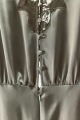 Vestido midi color verde oliva de tejido satinado, con cuello barco, mangas cortas abullonadas con puños y aplicación de encaje a contraste en la parte superior. Cierre trasero con cremallera oculta y botones forrados.