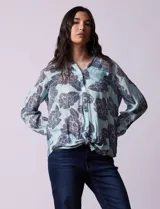 Camisa de gasa estampada a rayas verticales de color celeste, blanco, naranja y marrón. Tiene cuello con solapa, escote en V, abertura central con botones, bolsillo aplicado en el pecho y terminación anudada en la parte delantera.
