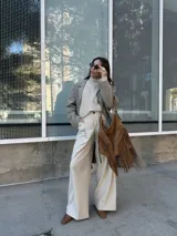 Bolso tipo hobo color tostado, hecho de cuero con flecos largos en el frente y dos bolsillos con cierre. Tiene una manija regulable con hebillas metálicas.