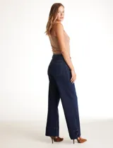 Jean wide leg azul oscuro de tiro alto, con pierna ancha y ruedo con tajo lateral. Presenta pretina con pasadores, botón y cierre, y bolsillos delanteros y traseros.