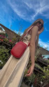 Bandolera pequeña tipo 'phone bag' de símil cuero color rosado pálido, con cierre de cremallera y correa ancha de tela con diseño de chevron en tonos claros.