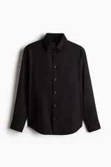 Camisa negra de manga larga con cuello clásico, tapeta con botones y bolsillo en el pecho. Corte regular.