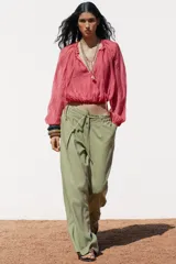 Pantalón ancho color verde oliva confeccionado en lino. Tiro alto con cintura elástica ajustable con cordón y pinzas delanteras. Presenta bolsillos laterales y traseros. Incluye cinturón de la misma tela con apliques metálicos.