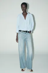 Camisa blanca de cuello solapa y manga larga con puños. Tiene un nudo en la parte delantera y cierre frontal con botones.