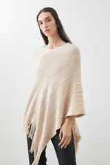 Capa color beige de tejido de punto con diseño de líneas en relieve y flecos en el borde inferior.