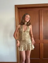 Vestido corto de lentejuelas color verde oliva, con escote en V, breteles finos cruzados en la espalda, cut-outs laterales y volado en el ruedo.