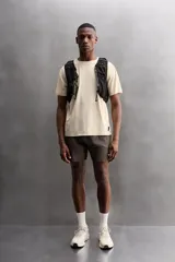 Camiseta deportiva marrón confeccionada en tejido técnico ligero y elástico con estructura perforada. Cuello redondo, manga corta y bajo asimétrico con aberturas laterales. Detalle de logo estampado.