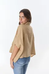 Camisa color beige de lino con cuello camisero, manga corta y cierre frontal con botones. Presenta detalles de encaje en el cuello, el frente y las mangas.