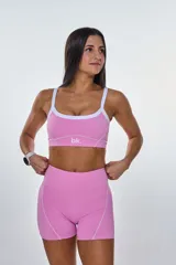 Conjunto deportivo rosa compuesto por un top con tirantes blancos y un short ajustado con costuras blancas.