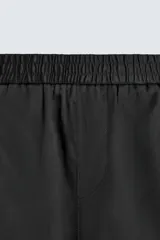 Bermuda negra de corte relajado, confeccionada en tejido satinado de viscosa. Presenta cintura elástica ajustable con cordón interior, bolsillos frontales y un bolsillo trasero de plastrón.