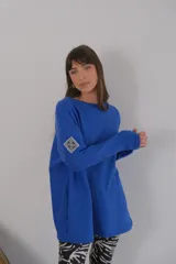 Buzo azul de viscosa con cuello redondo y manga larga. Presenta un aplique con diseño geométrico en el brazo izquierdo.