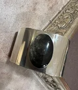 Brazalete rígido de alpaca plateada con piedra ovalada negra engarzada en el centro.