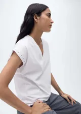 Camiseta gris con cuello en V, manga corta y detalle de tachuelas en los hombros.