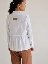 Camisa celeste de algodón con cuello clásico, cierre frontal con botones y mangas largas. Presenta volados en el frente y corte evasé.