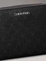 Billetera mediana negra con cierre perimetral y textura de monograma en relieve. Presenta el logo metálico de Calvin Klein en el frente y herrajes plateados.