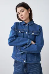 Campera clásica de jean color azul medio, con cuello clásico, cierre frontal con botones, bolsillos con solapa en el pecho y mangas largas con puños abotonados.