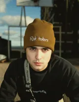 Gorro de lana sintética color marrón con bordado frontal de la frase "Risk takers" en color blanco.