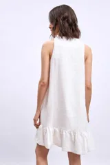 Vestido corto sin mangas, color celeste claro, con escote en V y un pequeño broche decorativo en la abertura frontal. Presenta un corte holgado tipo babydoll con bolsillos laterales y un ruedo con volado.