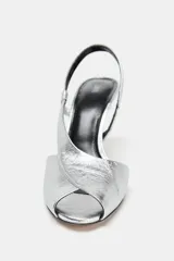 Sandalias plateadas de piel metalizada con puntera abierta, tiras cruzadas y cierre con tira trasera elástica. Tacón fino de 9,5 cm.