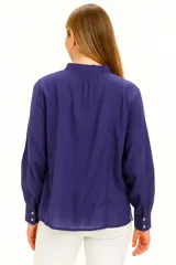 Blusa blanca de manga larga con cuello mao con lazo y cierre frontal con botones.