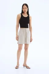Short color beige de tiro alto con cintura elástica fruncida con ribete de volado, cordón para ajustar fino con cuentas de metal y bolsillos laterales discretos.