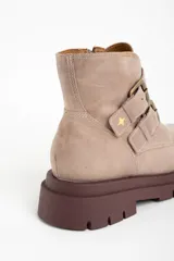 Bota corta de cuero color rosa viejo o beige claro, con suela track gruesa color marrón oscuro. Presenta dos tiras ajustables con hebillas metálicas color bronce y cierre lateral.
