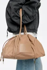 Bolso bandolera grande de nylon color beige, con estructura blanda, doble asa de tejido, logo grabado BIMBA Y LOLA, bolsillo interior con cierre y placa metálica logotipada.