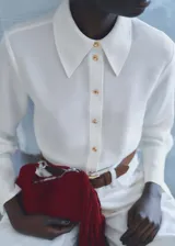 Camisa blanca de tejido fluido, con cuello camisero, cierre frontal con botones y mangas largas con puños abotonados.