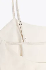 Top blanco con tirantes finos, escote recto y bajo asimétrico con volados.