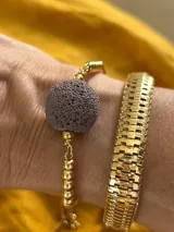 Pulsera dorada con tres piedras volcánicas negras y cierre corredizo.