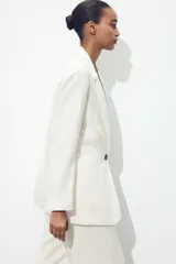Blazer fucsia de cuello solapa y manga larga con hombreras. Detalle de tejido efecto arrugado. Bolsillos delanteros de vivo. Cierre frontal con un botón.