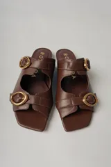 Sandalias planas de cuero color marrón con dos tiras anchas sobre el empeine, cada una con hebilla dorada.