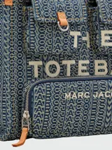Bolso tote mediano de denim con monograma de la marca Marc Jacobs, con doble asa de mano de cuero y correa bandolera ajustable de tela.