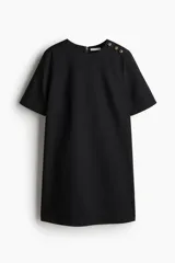 Vestido corto negro con cuello redondo y abertura de cerradura con botón oculto en la nuca. Modelo de manga corta con pinzas en el busto y bajo recto.