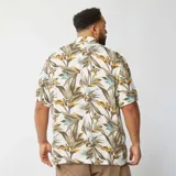 Camisa de manga corta con estampado de hojas en tonos verdes, marrones y celestes sobre fondo blanco.