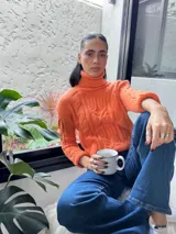 Polera elastizada color naranja con cuello alto y diseño trenzado.