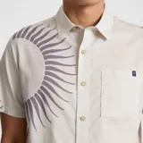Camisa de manga corta color crema con estampado de soles en color gris. Tiene cuello clásico, cierre con botones y un bolsillo en el pecho.