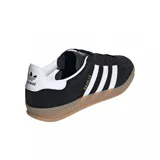 Zapatillas Adidas Gazelle Indoor negras con las tres tiras blancas y suela color caramelo.