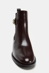 Botín de cuero color marrón oscuro, estilo Chelsea, con elásticos laterales, hebilla decorativa en la caña, tirador trasero y tacón bajo cuadrado.