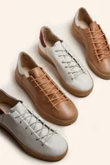 Zapatillas bajas blancas de cuero vacuno con detalle de refuerzo de gamuza color borgoña en el talón y suela de goma color caramelo.