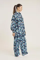 Conjunto de camisa de manga larga con botones y pantalón de corte recto, ambos con estampado de hojas y flores en tonos azul y naranja sobre fondo azul marino.